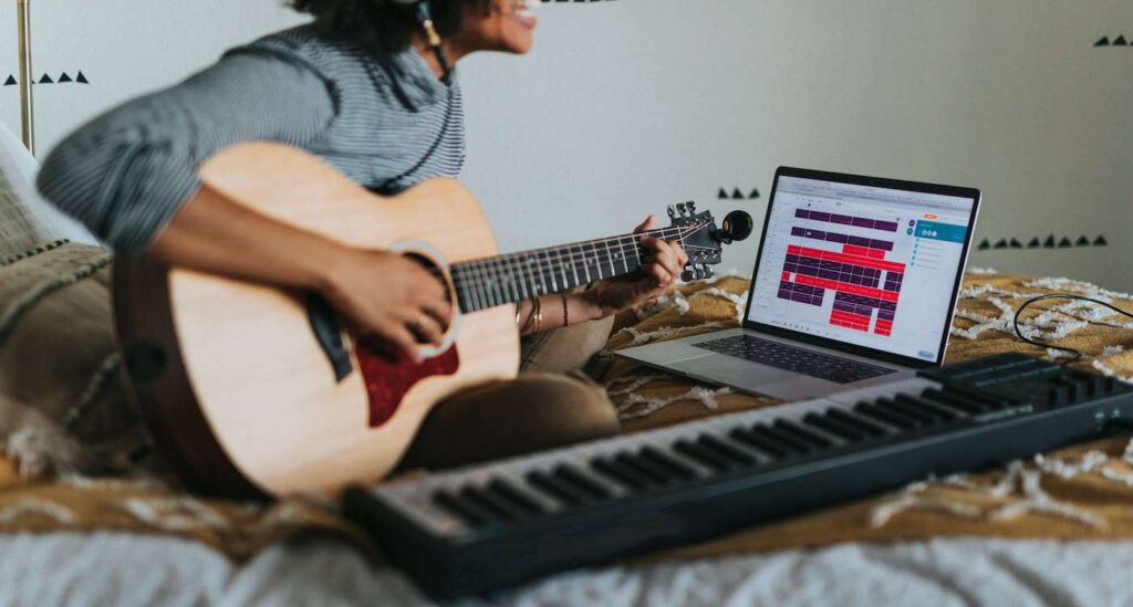 Person singing and playing guitar while recording on a laptop.