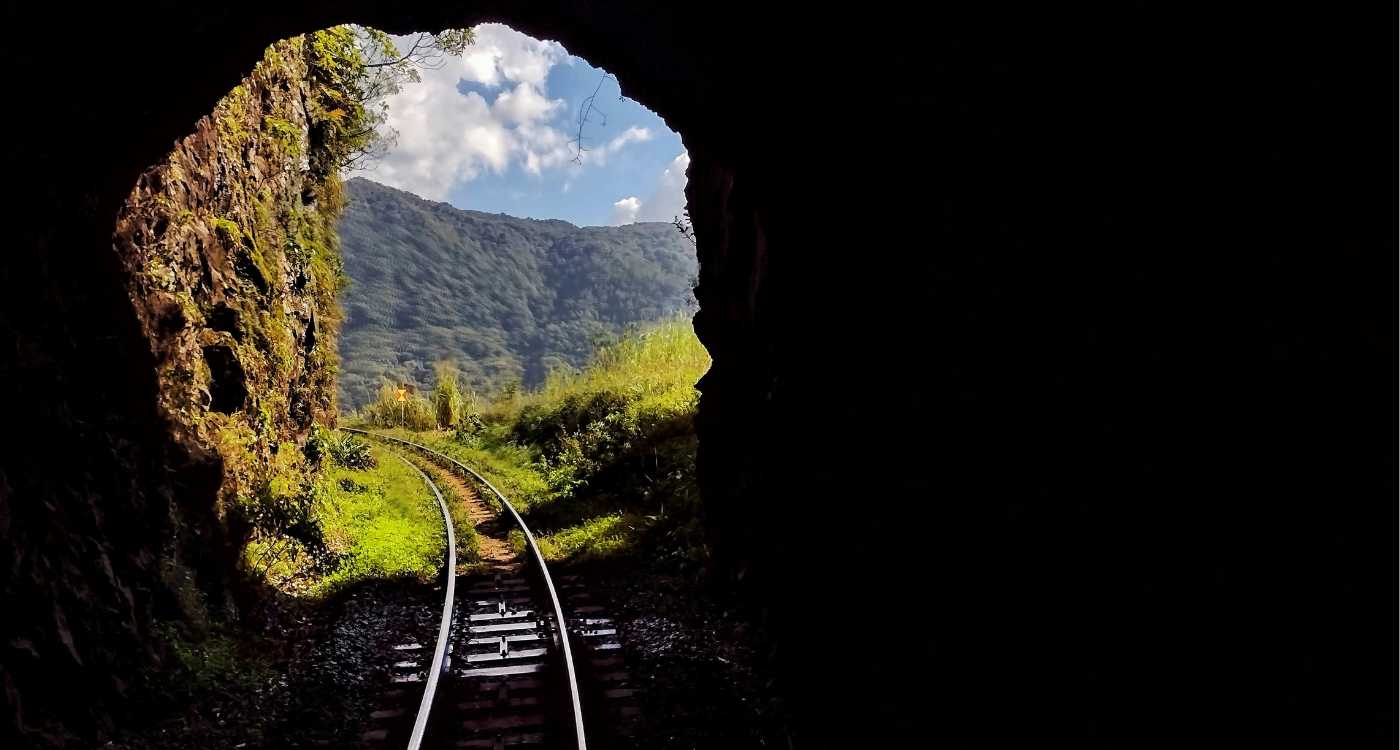 Image of train tracks emerging from a tunnel into a mountainous landscape.