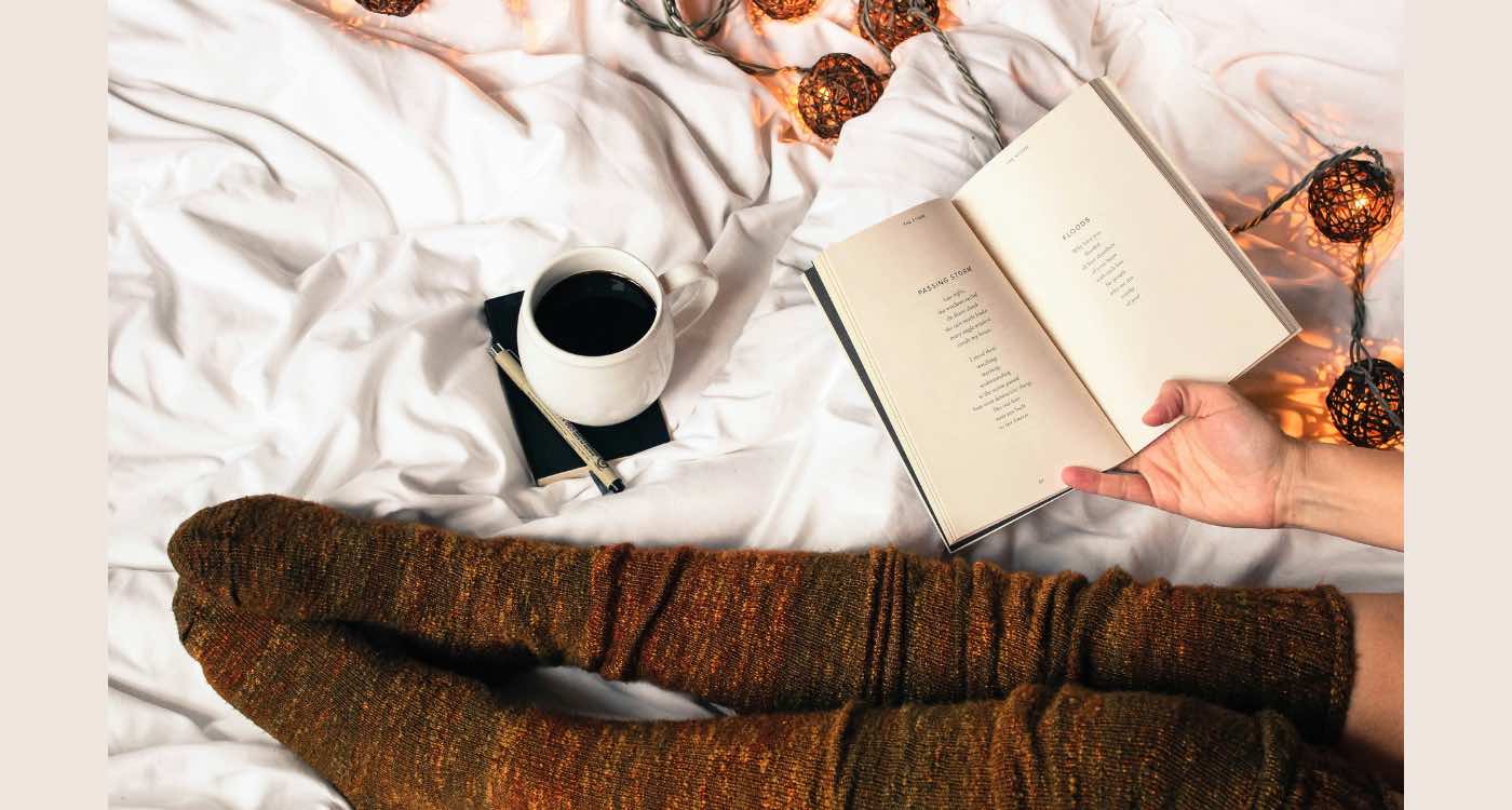 photo of a bed, a book, socks and coffee.