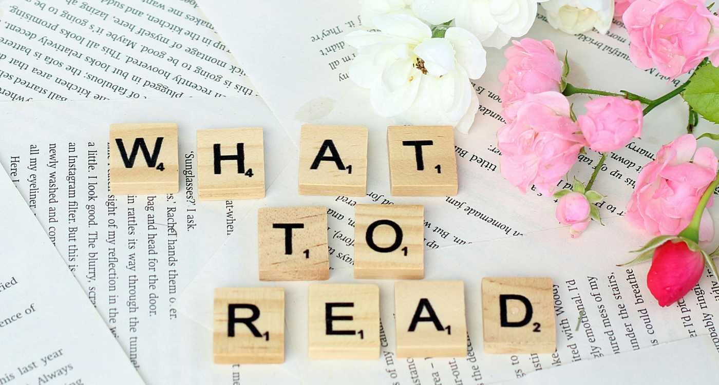 Flowers and Scrabble tiles spelling out "What to read" on top of open book pages.