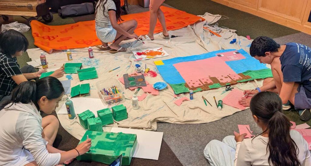 Six teen summer volunteers sitting on the floor and painting decorations for the 2025 TSV Minecraft Mania event.