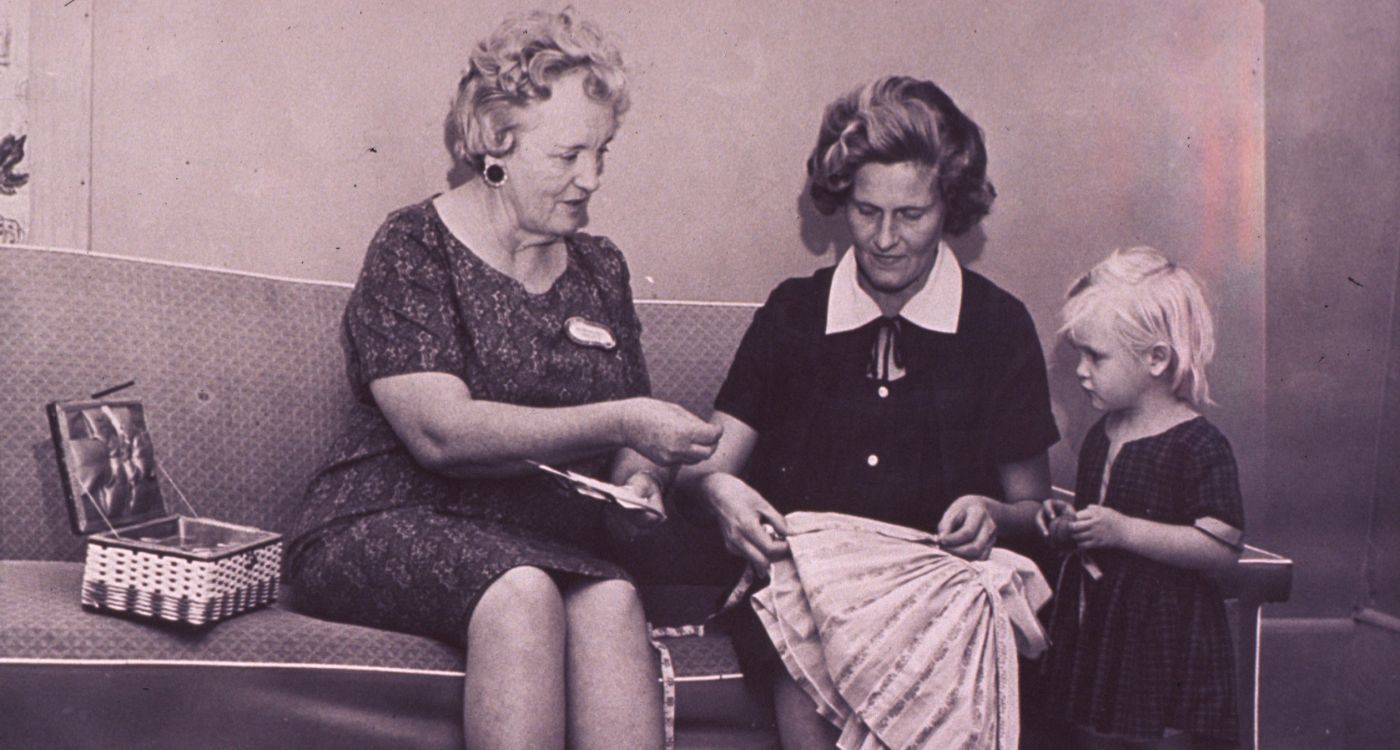 A black and white image of two women and a child sewing a dress.