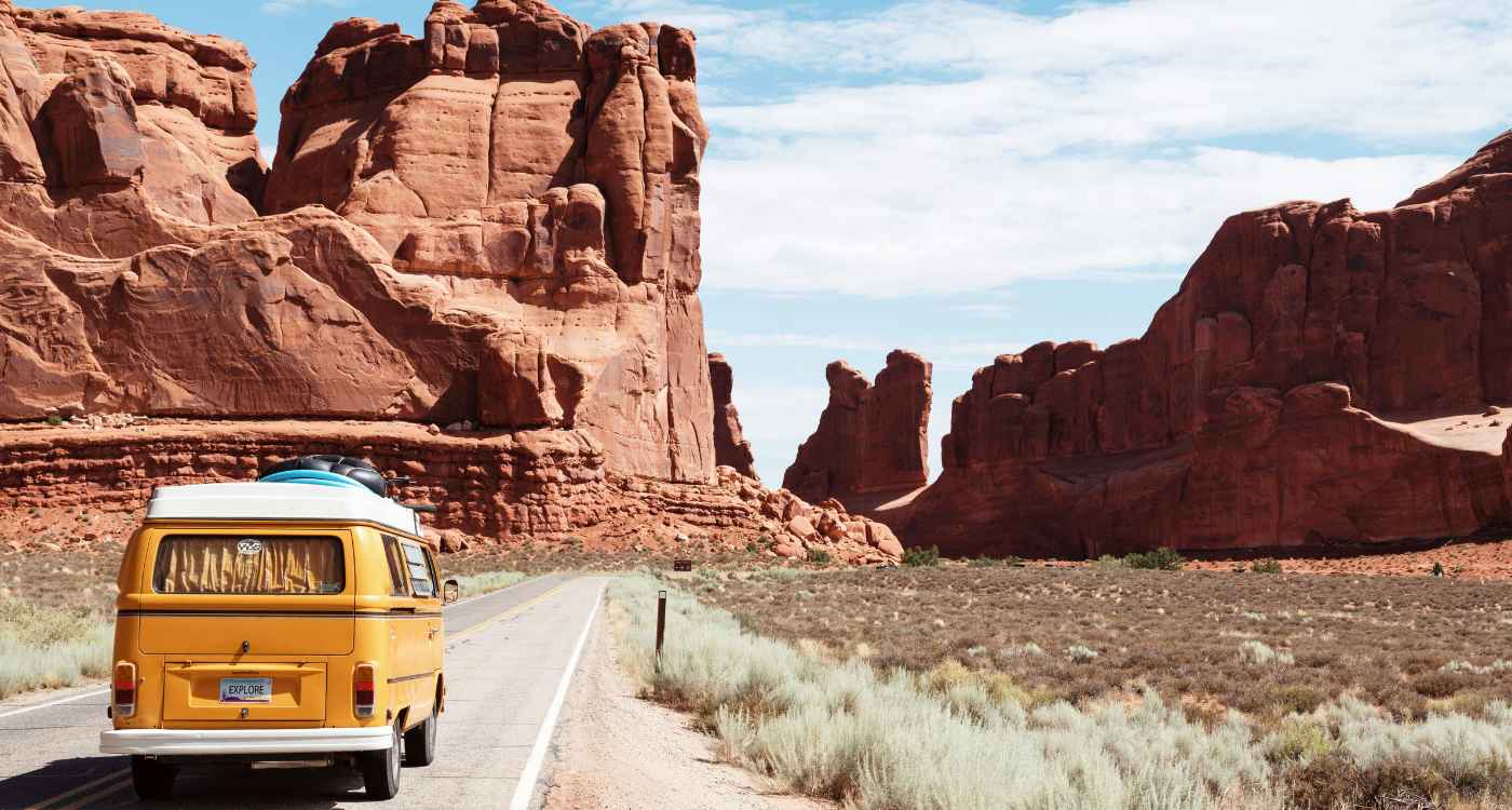 Image of a yellow van driving into a desert landscape with dramatic rock formations